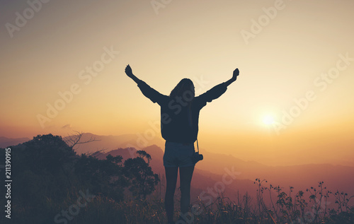 Silhouette Happy female with camera hiking on the high cliffs at sunrise