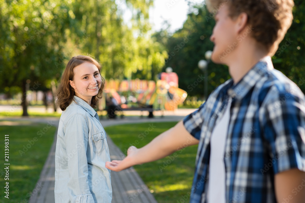 In the summer in park in nature. The young man gets acquainted with the girl. She stretches out her hand for communication. The girl smiles happily says yes. Dating in the city.
