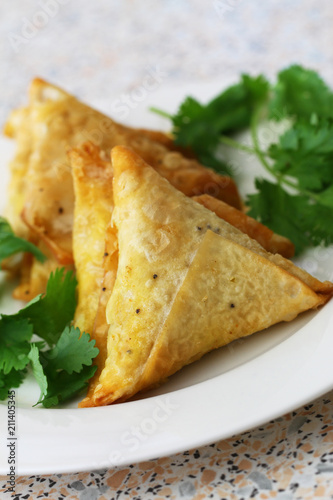 Indian deep fried vegetarian samosas on plate and fresh coriander
