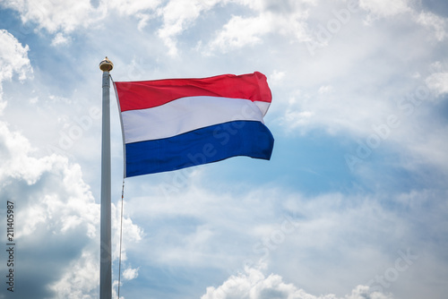 Dutch royal flag in the sky/ flag of the netherlands in the wind on a flagpole against a background of clouds in the sky
