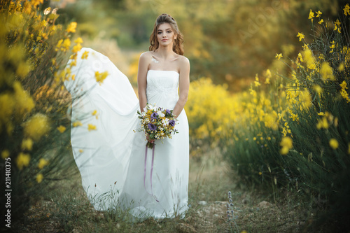 Pretty young bride with bouquet of wildflowers in yellow field