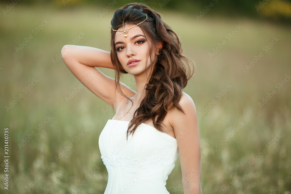 Portrait of beautiful happy young bride is wearing head decor in field over sunset lights