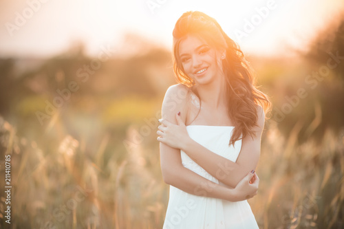 Portrait of beautiful happy young bride in field over sunset lights