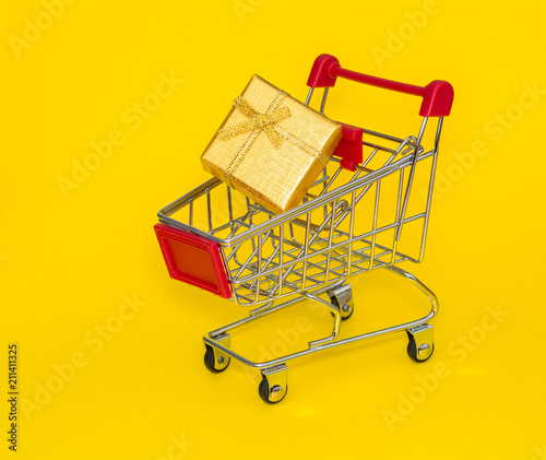 Shopping trolley with gold gift on a yellow background