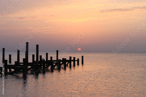 Sunrise on the sea. The sky is painted in shades of pink. Wooden piles of destroyed pier sticking out of the water. Early in the morning the sun appeared over the horizon of Red sea.