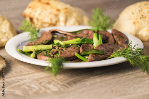 lamb liver food with green vegetables in the plate and local bread on the wooden table for restaurant and kitchen concept.