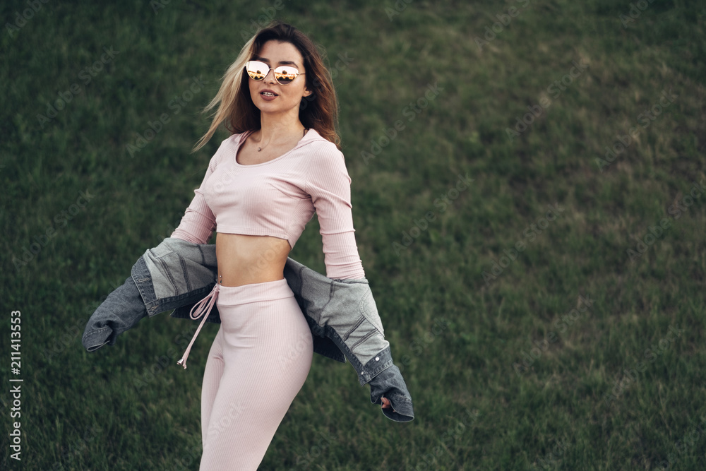 Portrait of Young and Beautiful Woman in Casual Clothes in the Street. Dressed in Pink Shirt and Pants. Spring, Summer Concept. Relax Time. Girl with Sunglasses. Enjoy City Sunset. Portrait of Young and Beautiful Woman in Casual Clothes in the Street. Dressed in Pink Shirt and Pants. Spring, Summer Concept. Relax Time. Girl with Sunglasses. Enjoy City Sunset.