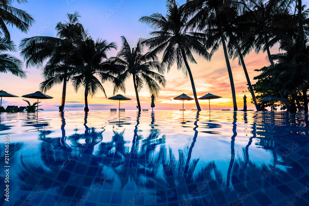 Fototapeta premium Summer beach holiday vacation destination, luxurious beachfront resort swimming pool with tropical landscape, quiet warm sunset, silhouette and reflection in water