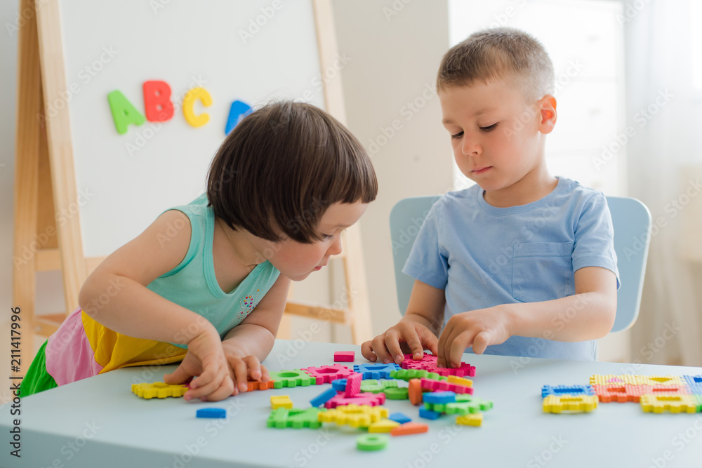 A boy and a girl collect a soft puzzle at the table. Brother and sister have fun playing together in the room. Preschool children and educational toys A boy and a girl collect a soft puzzle at the table. Brother and sister have fun playing together in the room. Preschool children and educational toys