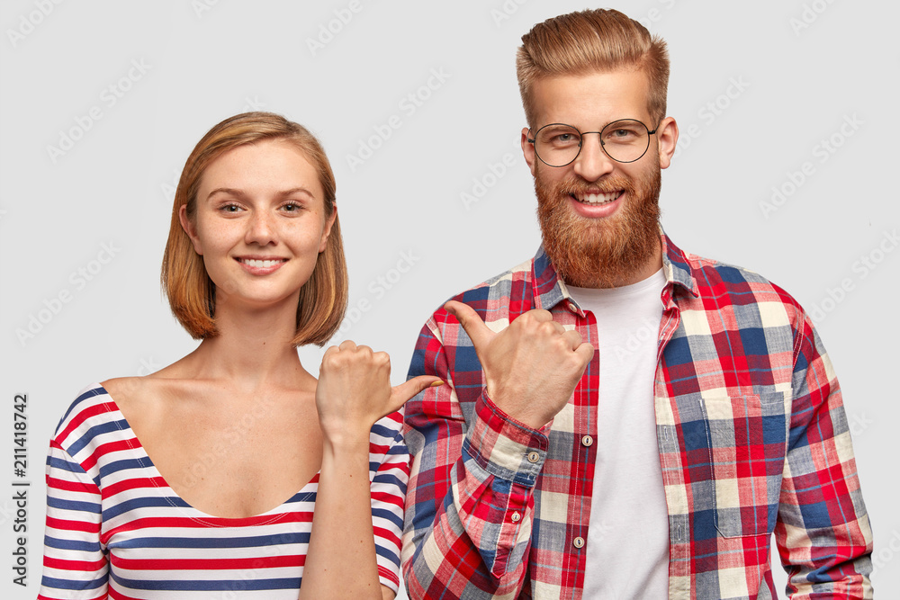 Joyful female and male best friends indicate at each other, have friendly smiles on faces, attract attention, stand closely, isolated over white background. Satisfied bearded man with girlfriend Joyful female and male best friends indicate at each other, have friendly smiles on faces, attract attention, stand closely, isolated over white background. Satisfied bearded man with girlfriend