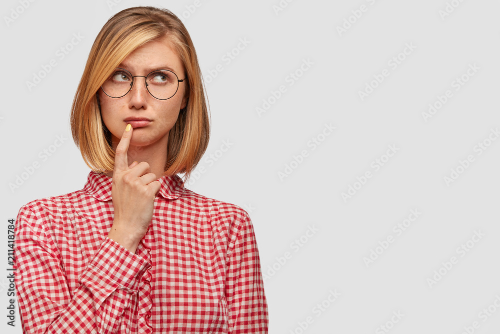Displeased Caucasian female with bobbed haircut, looks pensively upwards, has miserable expression, dreams about something desirable, doesn`t have any hope it come true, poses against white wall Displeased Caucasian female with bobbed haircut, looks pensively upwards, has miserable expression, dreams about something desirable, doesn`t have any hope it come true, poses against white wall