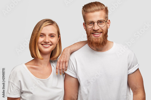 Portrait of cheerful young female and male friends have fun together, dressed in casual outfit, isolated over white background. Positive female with bobbed hairstyle and her bearded companion
