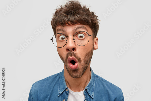Shocked stupefied bearded male drops jaw, stares with bugged eyes, wonders latest news about close friend, can`t beleive in his serious disease, isolated over white background. Emotions concept © Wayhome Studio