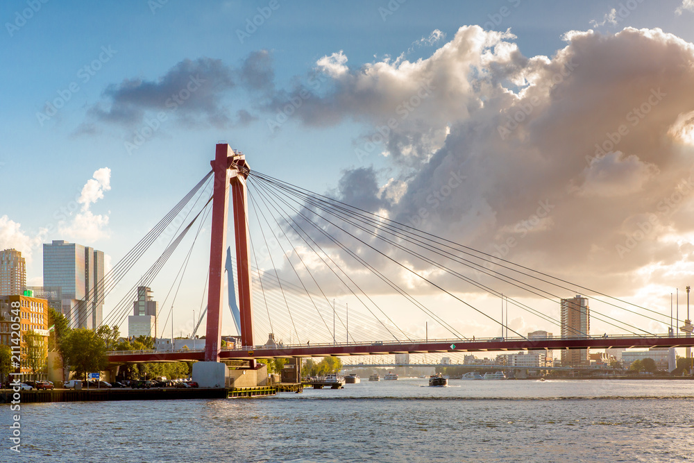 Sunset cityscape of Rotterdam with a highway bridge in the foreground, and downtown and the famous Erasmus bridge in the background against a blue sky