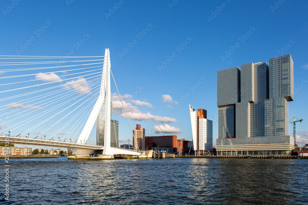 Cityscape of Rotterdam, The Netherlands, with the Erasmus bridge and high rise buildings of the financial district seen from the water against a clear blue sky