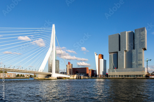 Cityscape of Rotterdam  The Netherlands  with the Erasmus bridge and high rise buildings of the financial district seen from the water against a clear blue sky
