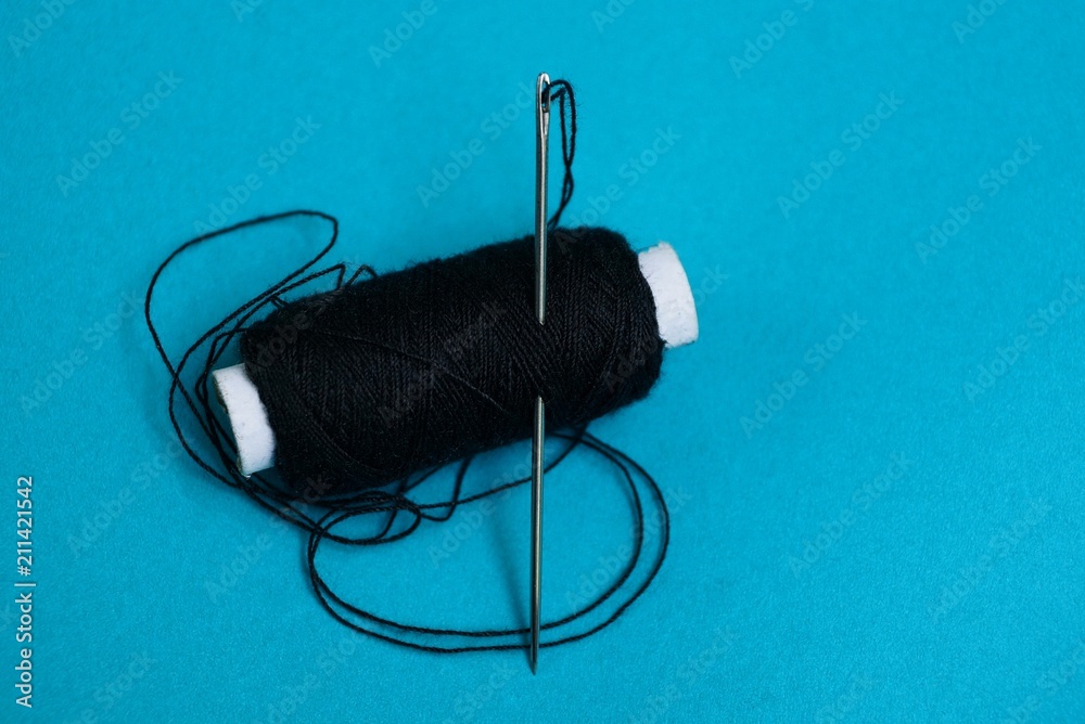 A long needle with a thread in a reel with black threads on a blue background A long needle with a thread in a reel with black threads on a blue background