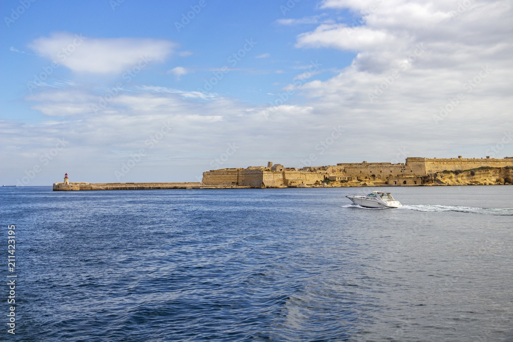 A motorboat passes along the Ricasoli Fort and Ricasoli Breakwater Lighthouse