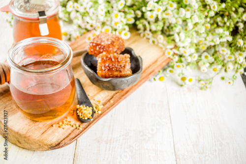 Organic floral honey, in jars, with pollen and honey combs, on a white wooden table, with wildflowers, copy space