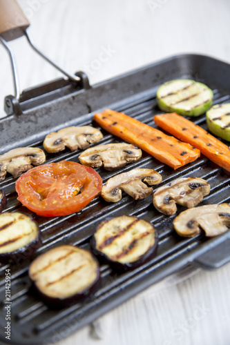Grilled vegetables in a grilling pan on a white wooden background, side view. Close-up.