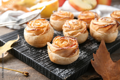 Wooden board with apple roses from puff pastry on table, closeup