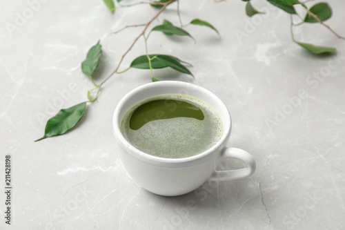 Cup of matcha tea and leaves on light background