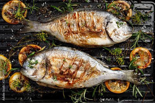 Grilled Dorada fish, sea bream with the addition of spices, herbs and lemon on the grill barbecue, top view photo