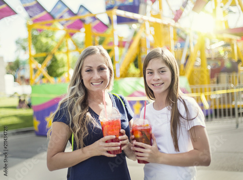Two happy girls drinking a sweet beverage at an amusement park or summer carnival. Enjoying a cool drink on a warm summer evening