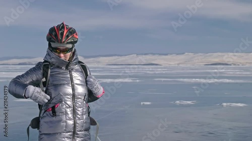 Woman is wearing sports equipment. The girl is dressed in a silvery down jacket, cycling backpack and helmet. Ice of the frozen Lake Baikal. The tires on the bicycle are covered with special spikes photo