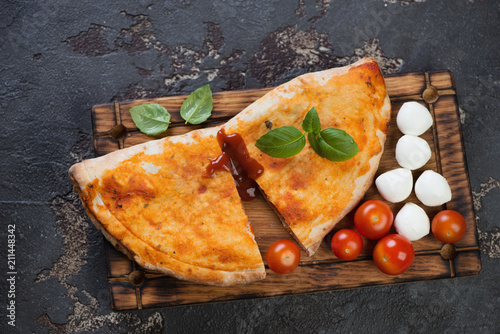 Rustic wooden serving tray with sliced pizza calzone over brown stone background, view from above, horizontal shot