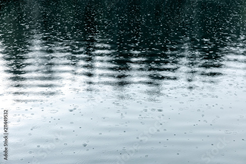 raindrops rippling on lake with trees reflecting in water during bad wether