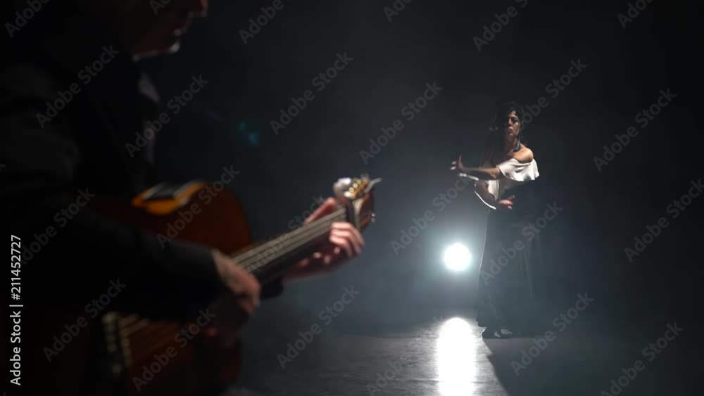 Flamenco. Girl dances her hands to the song the guitarist. Light from behind. Smoke black background Flamenco. Girl dances her hands to the song the guitarist. Light from behind. Smoke black background