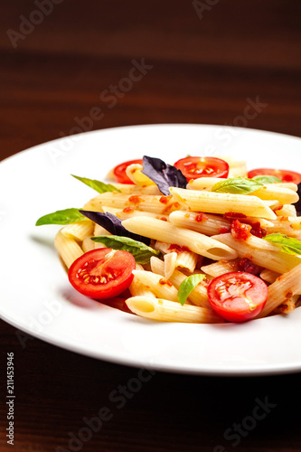 Penne pasta in tomato sauce with tomatoes and basil in a white forvor plate on a wooden table, next to the fork. Background image. concept of cooking Italian pasta for recipes. copy space, top view