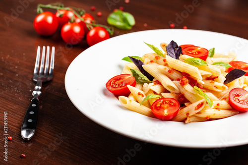 Penne pasta in tomato sauce with tomatoes and basil in a white forvor plate on a wooden table, next to the fork. Background image. concept of cooking Italian pasta for recipes. copy space, top view