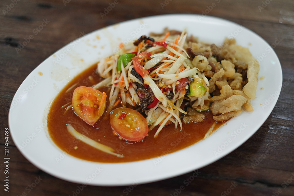 spicy papaya salad with salted crab  in white plate on wooden background