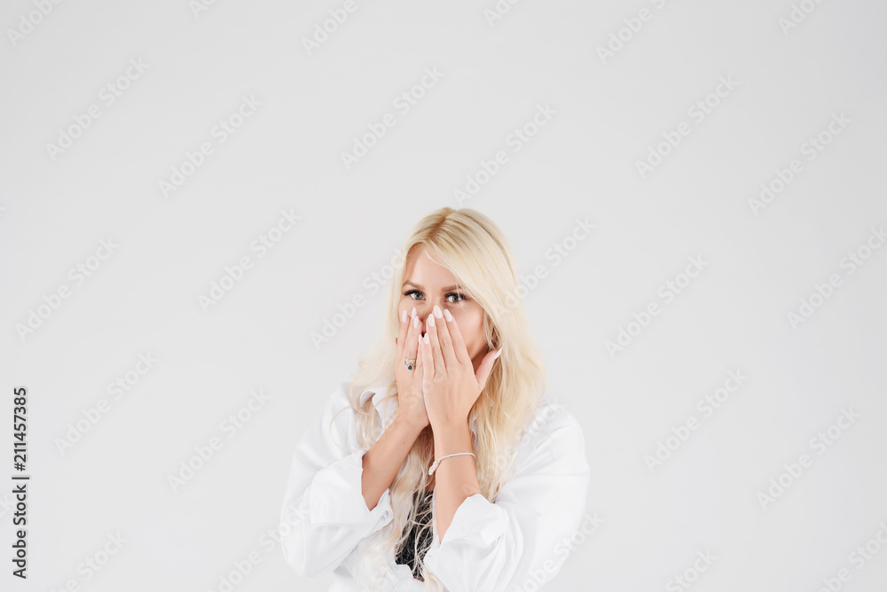 Happy blond women standing with hands near opened mouth and popping eyes. Girl with long hair in a white shirt on white isolated background in studio Happy blond women standing with hands near opened mouth and popping eyes. Girl with long hair in a white shirt on white isolated background in studio