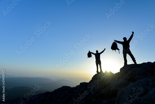 Hiker with backpack standing on top of a mountain with raised hands and enjoying view