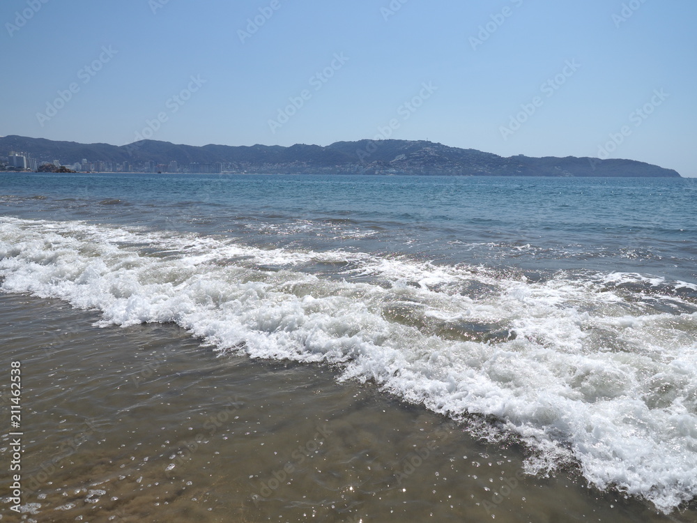 Beautiful view of sandy beach at bay of ACAPULCO city in Mexico with tourists and white waves of Pacific Ocean