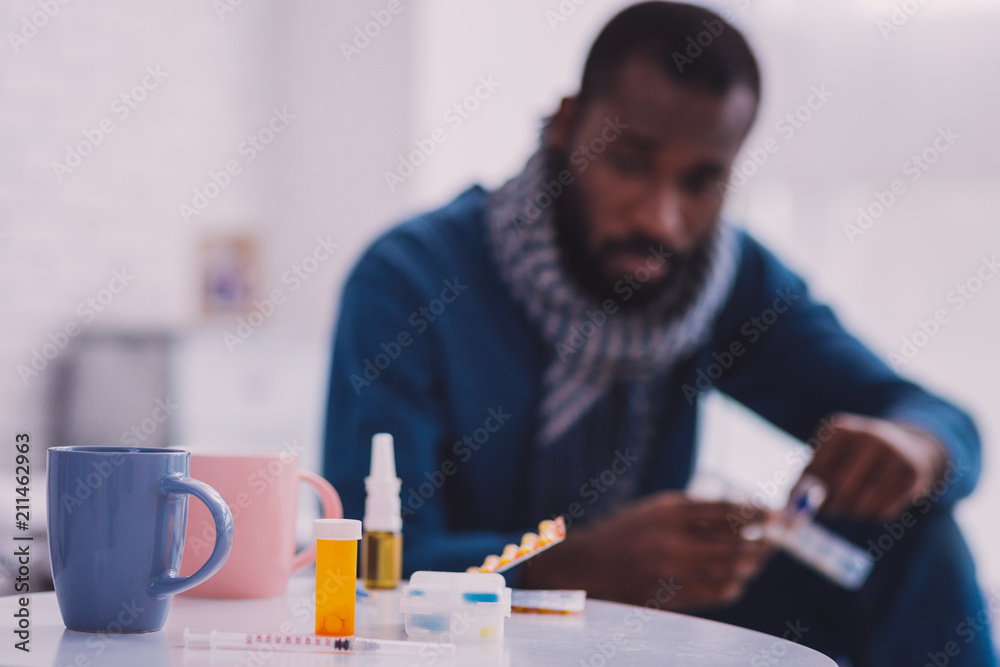It is mine. Thoughtful dark-skinned man sitting on the bed and looking at medicine It is mine. Thoughtful dark-skinned man sitting on the bed and looking at medicine