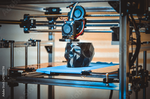 3D printer printing a model in the form of black skull close-up. The 4ht industrial revolution. Automatic three dimensional performs plastic modeling. Progressive modern additive technology photo