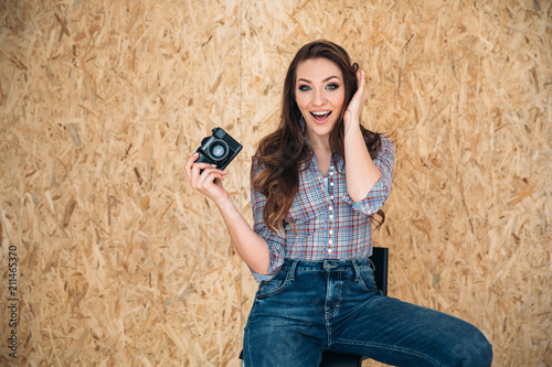 A nice and satisfying shining woman sits on a chair in everyday jeans and a shirt, she is happy, because she just made an excellent shot on her camera. photo