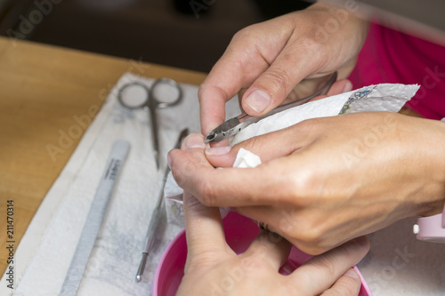 Closeup of manicure applying, cutting the cuticle with scissors. Woman in nail salon receiving manicure by professional beautician. Manicure process in beauty salon, close up