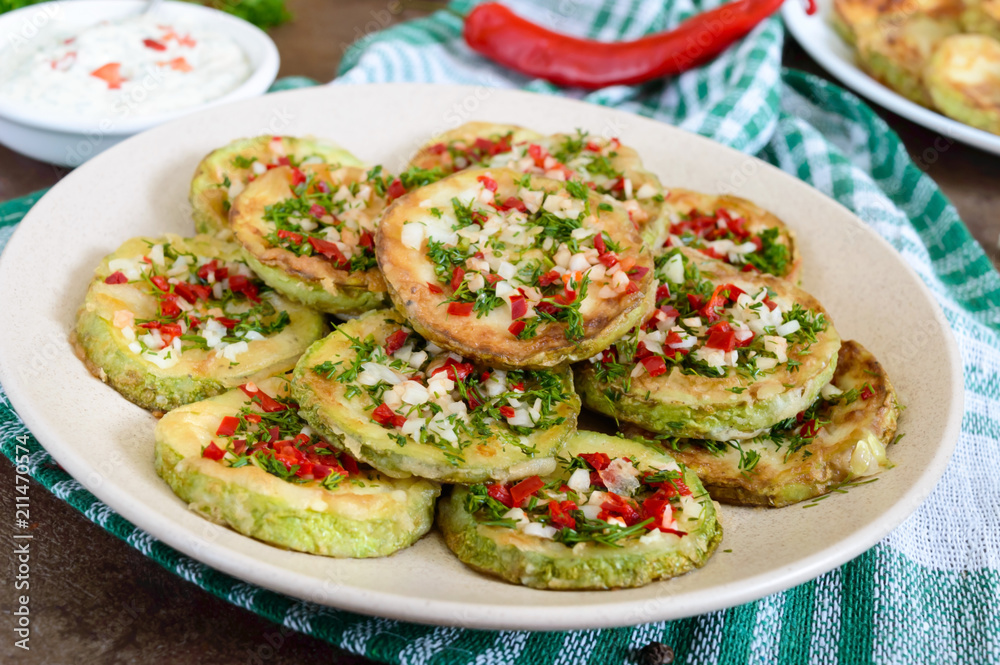 Fried circles of young zucchini with garlic, red pepper, greens on a plate. Vegetarian menu. Fried circles of young zucchini with garlic, red pepper, greens on a plate. Vegetarian menu.