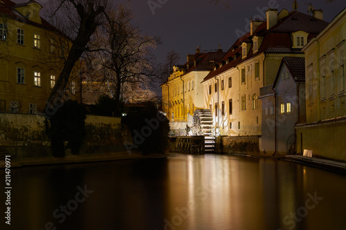 Old water mill on canal in little quarter of old town of Prague, capital of Czech Republic taken in winter night with snow on the  mill Wheel, populr view between tourist photo