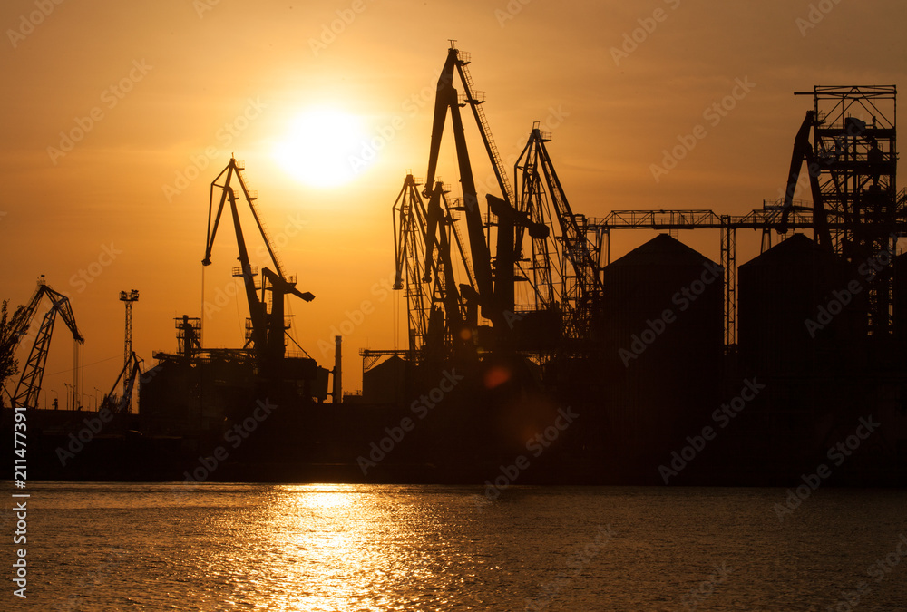 sea cranes in the back light in the evening against the backdrop of the sea and the setting sun in the seaport