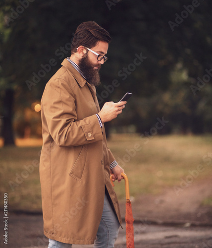 A handsome hipster modern man uses a smartphone on a rainy day