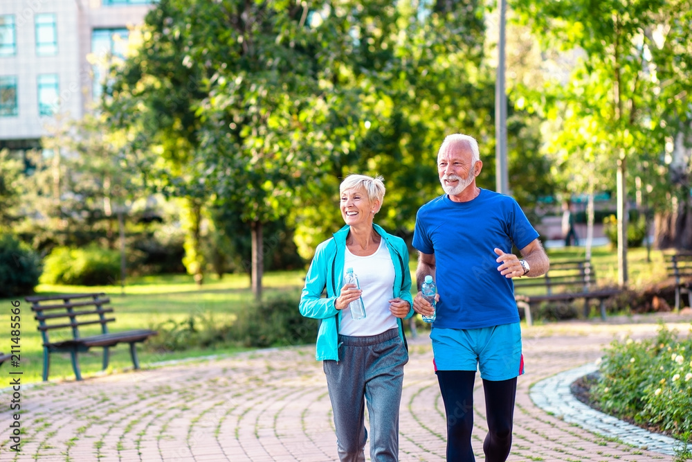 Obraz premium Happy senior couple jogging outdoors in park.
