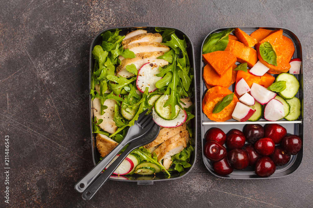 Healthy meal prep containers with grilled chicken with salad, sweet potato, berries, fruits and vegetables. Dark background, top view.