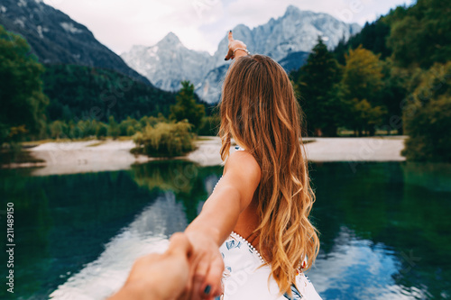 Attractive young woman holding hand of her friend and walking next to the lake photo