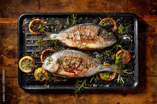 Grilled  fish, sea bream, dorada with the addition of spices, herbs and lemon on the grill plate located on a wooden background,  top view. Healthy eating concept